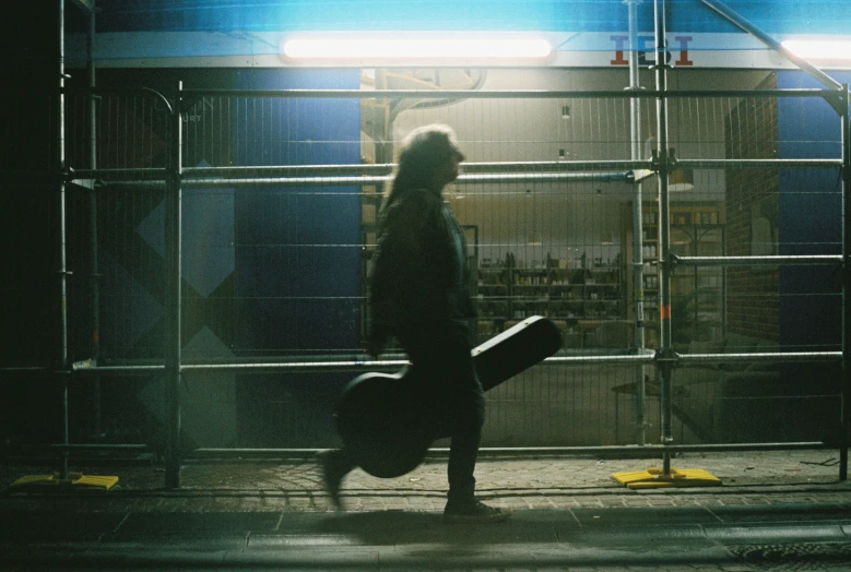 man walking on city sidewalk holding luggage in dark area