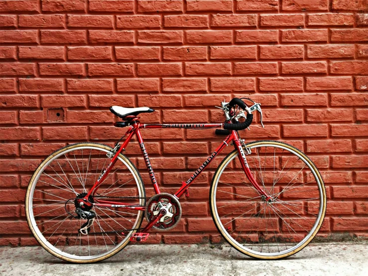 an old red bicycle parked against a brick wall