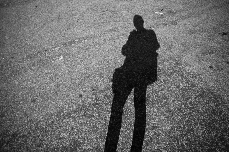 a shadow of a man holding an umbrella standing in the road