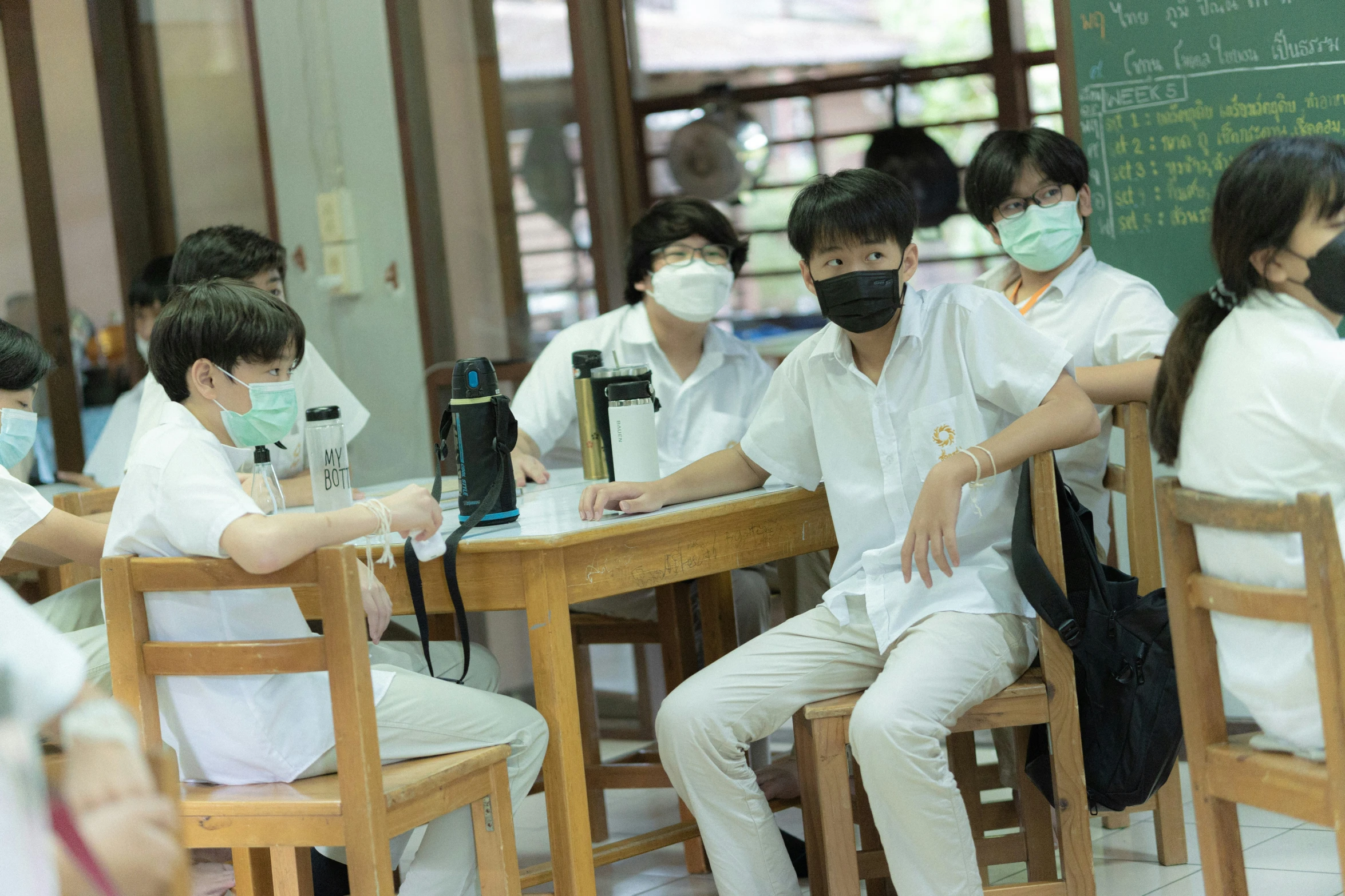 people in masks sit at small tables working on electronics