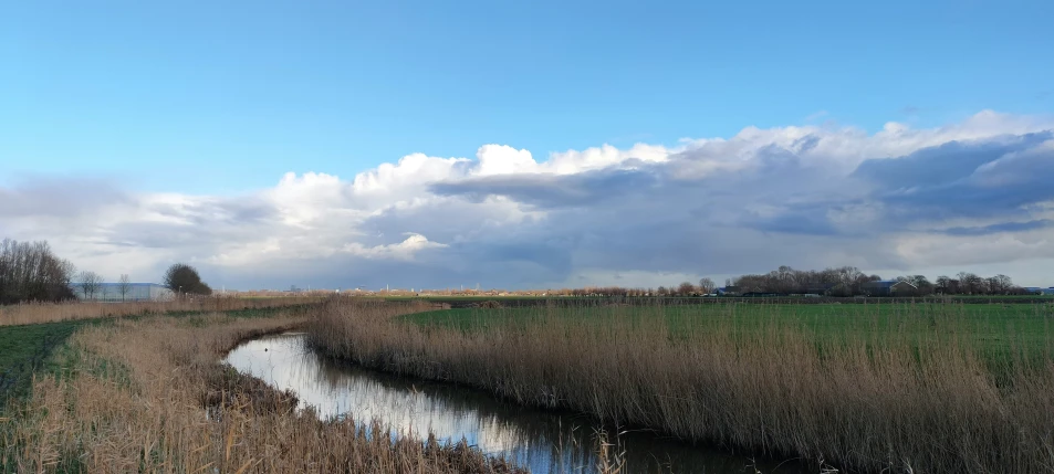 small stream running through the grassy field in front of a cloudy sky