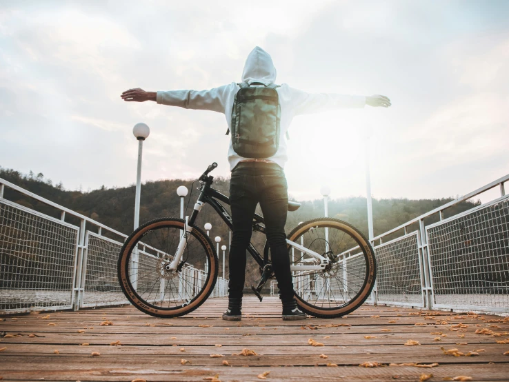 man in hoodie standing with two bicycle next to each other