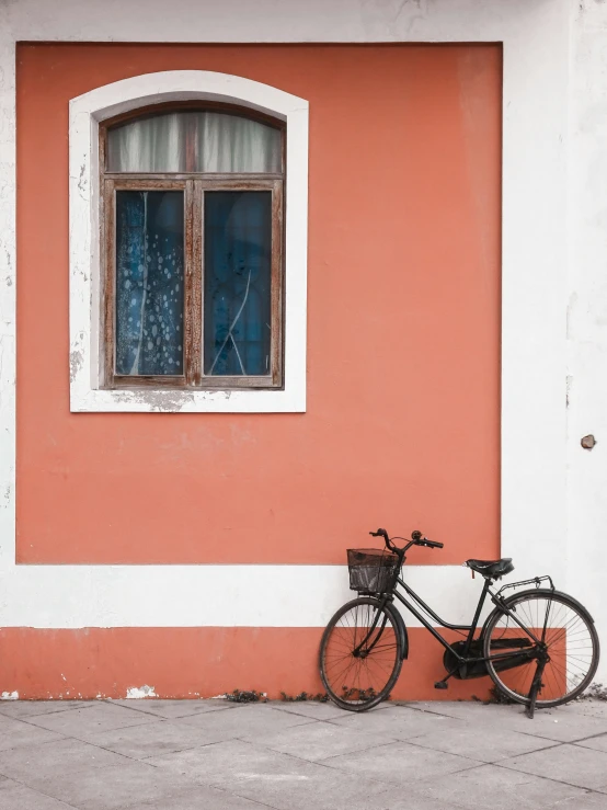 a bicycle leans against a colorful wall while a bike leans against a window