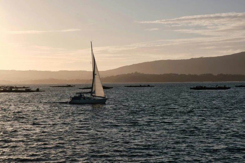 a sailboat in the ocean with other ships behind it