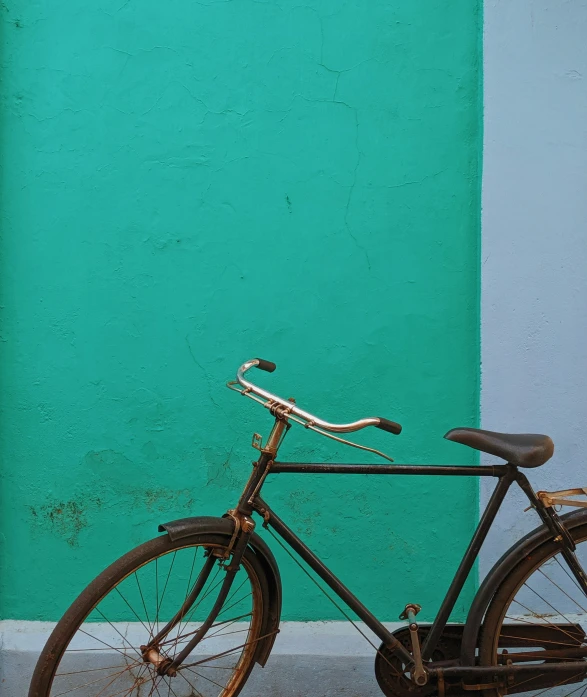 a rusty bike parked in front of a green wall