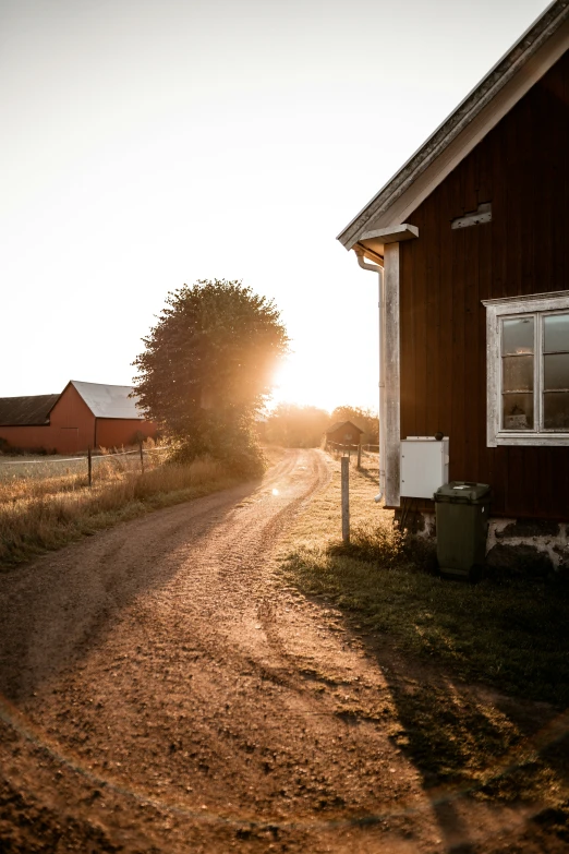 the sun is setting on the farm and a road goes through the barn door