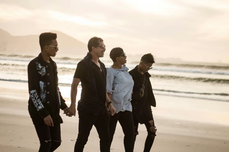 four young men holding hands walking along the beach