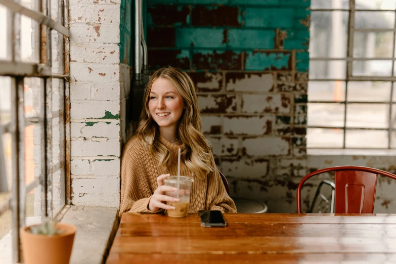 a young woman is sitting at a wooden table in a restaurant holding a drink