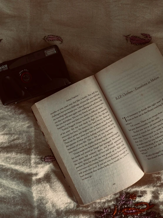 an open book and an analog camera sit on a bed