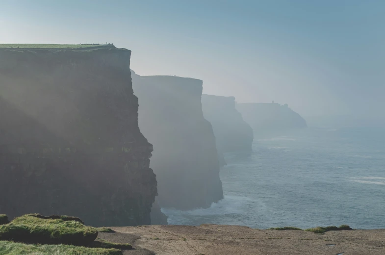 people at the edge of a cliff overlooking an ocean and cliffs