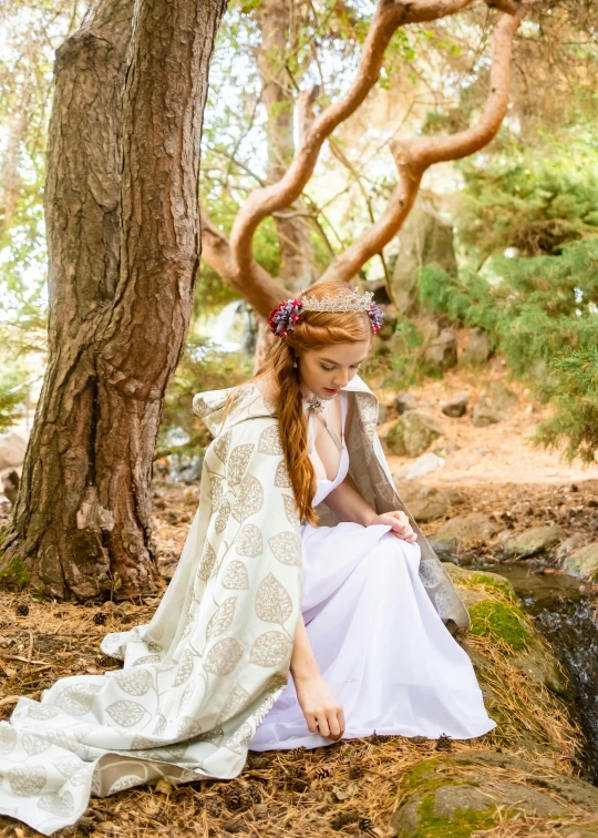 a young woman wearing a long dress sitting in the woods