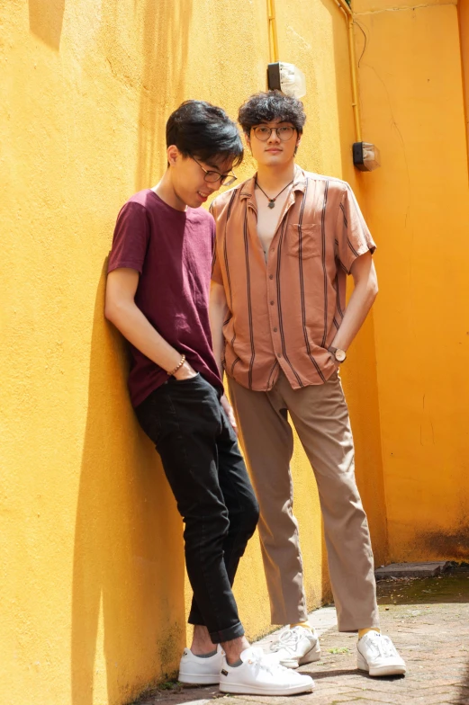 two boys pose for a picture while leaning against a yellow wall