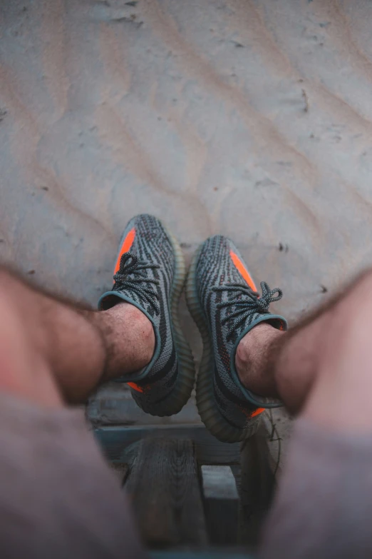 the feet of two people in a black and orange shoe standing on boardwalk