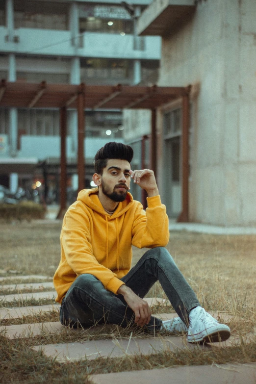 a man sits on the ground wearing a yellow sweater