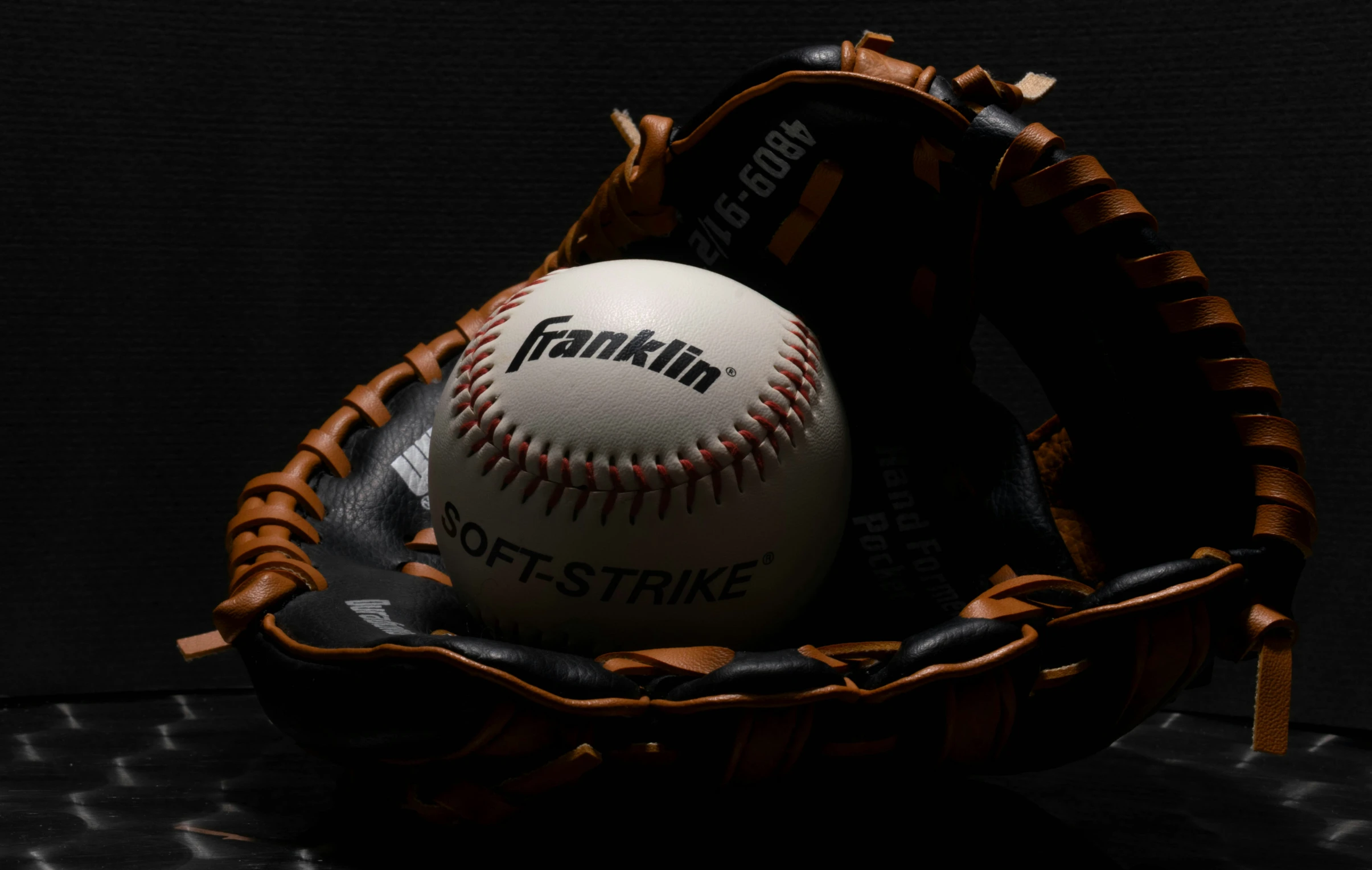 a baseball and glove on a dark surface