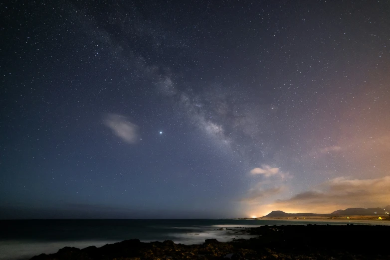 a night sky with several bright stars and the ocean in front of it