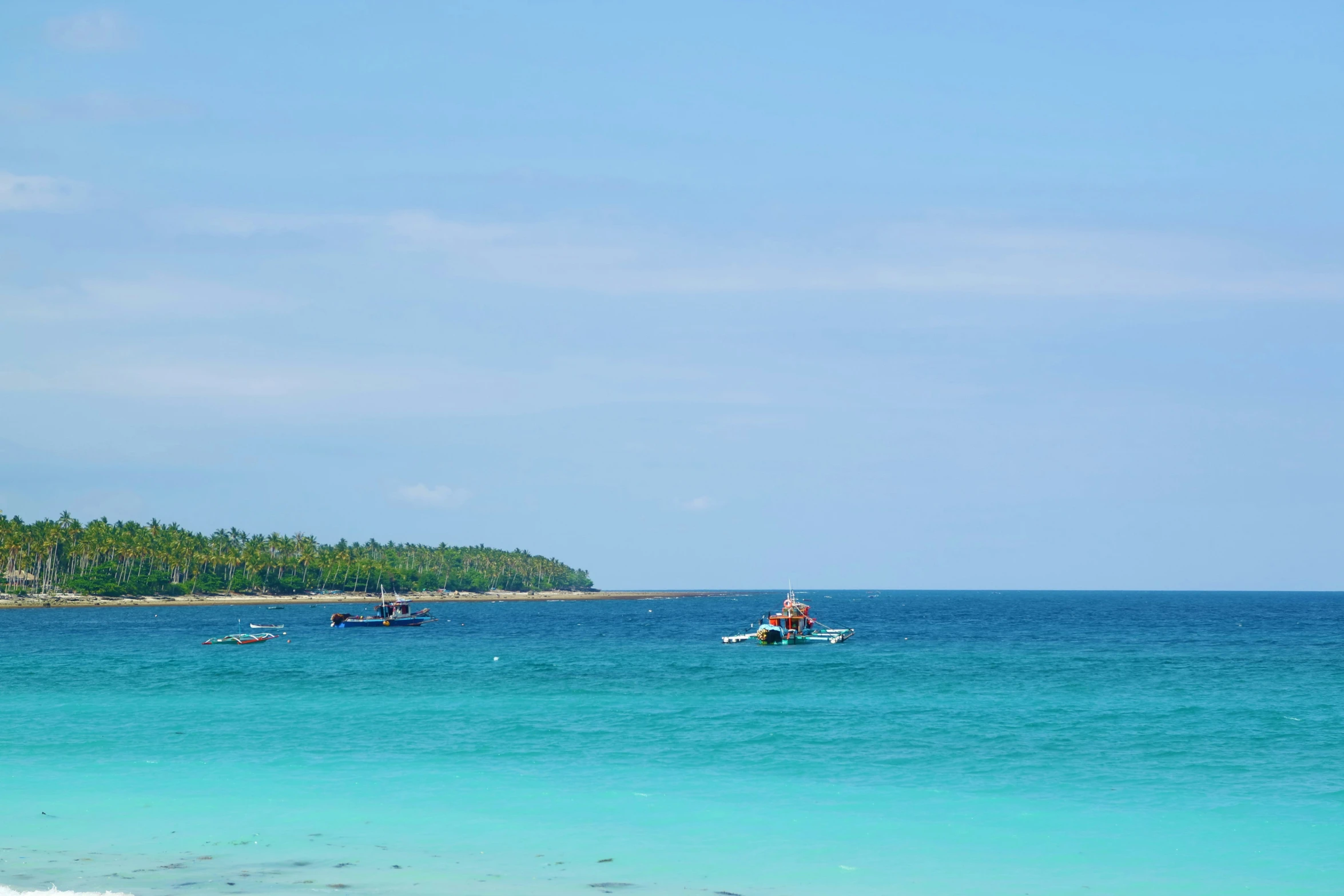 blue ocean with boats and small island on far side