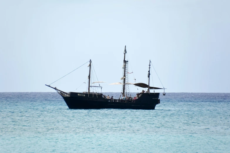 a small black ship floating in the middle of the ocean