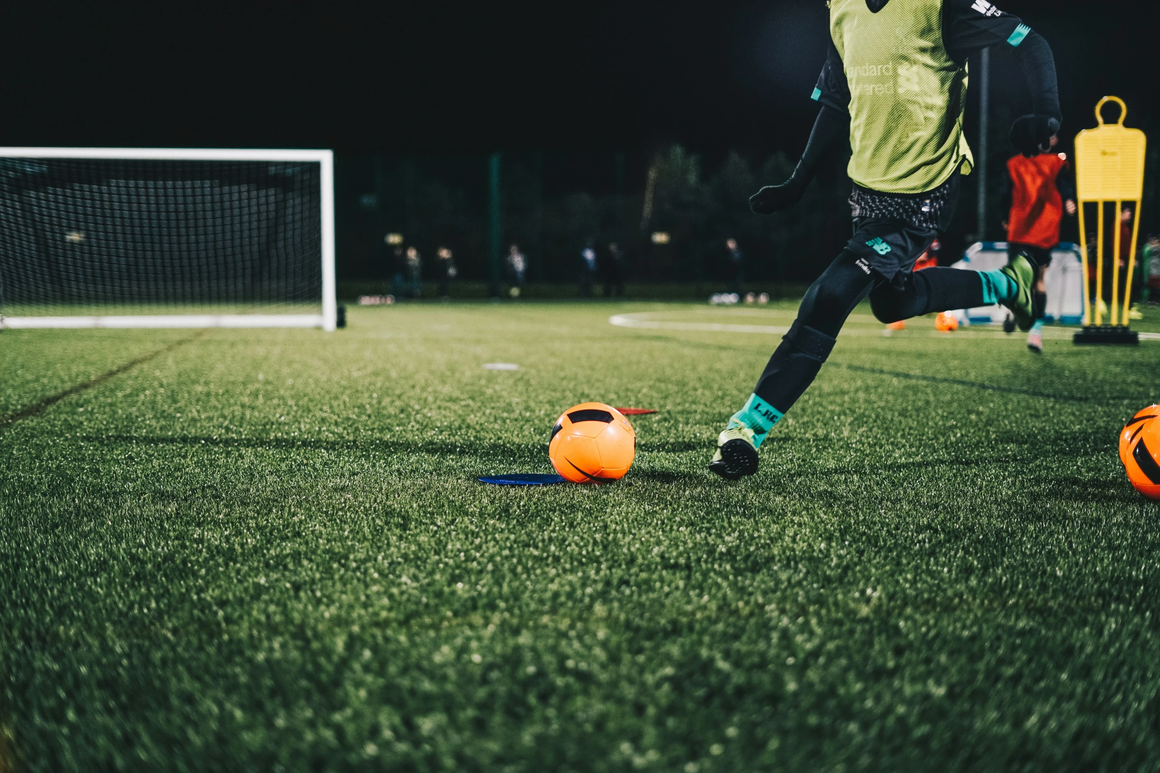 soccer ball being dribble by man kicking it on grassy field at night