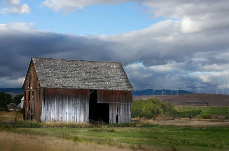 an old barn is out in the field with a storm