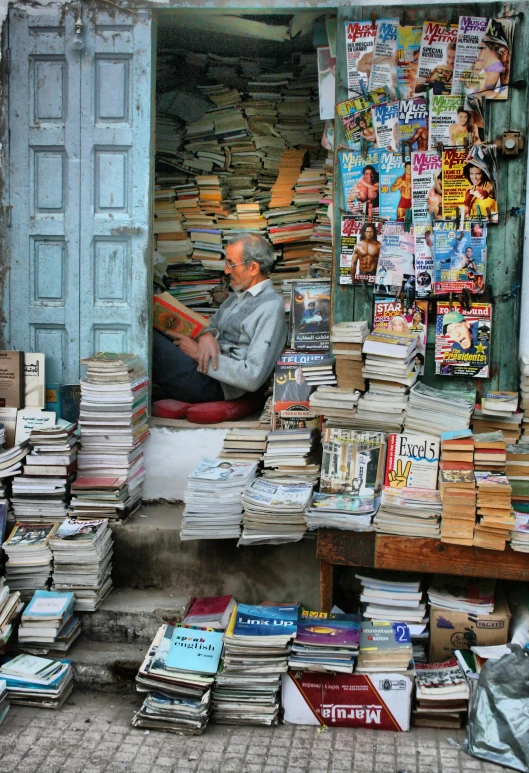 a person sitting down in a doorway with a lot of books on the sidewalk