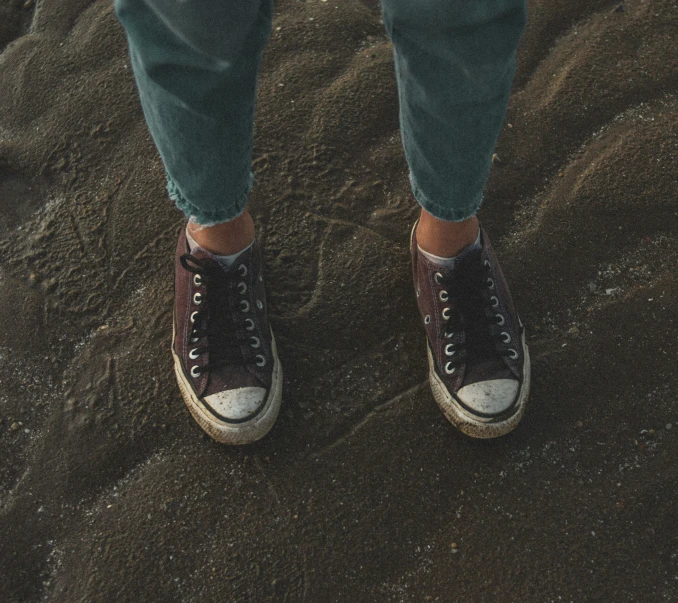 a man's legs and ankles standing in sand with shoes