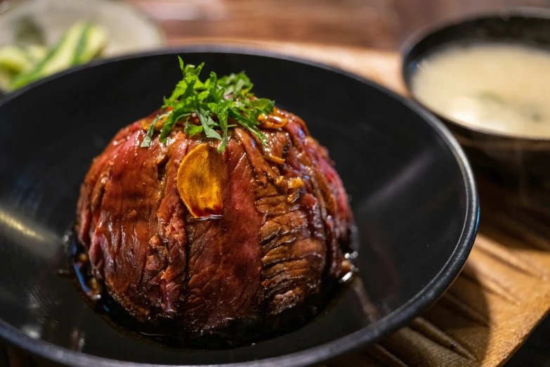 the black bowl holds a red colored meat and green vegetables