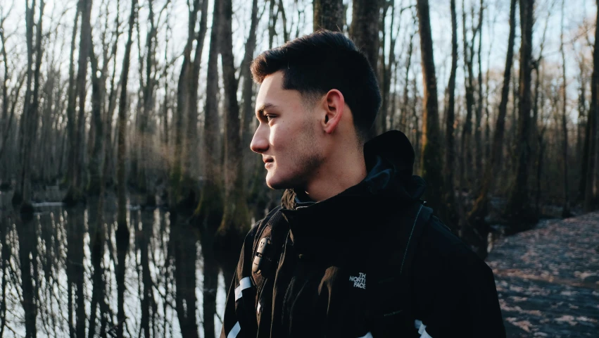 a man standing next to water surrounded by tall trees