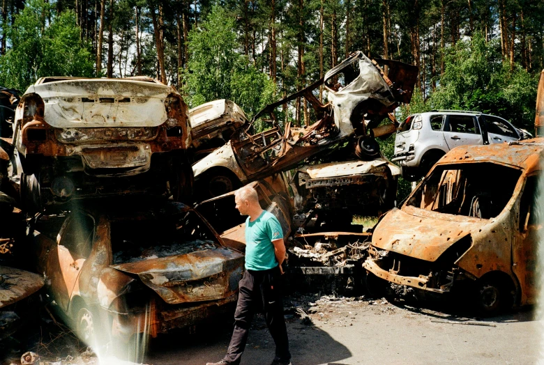 two men stand near old cars in a scrap yard