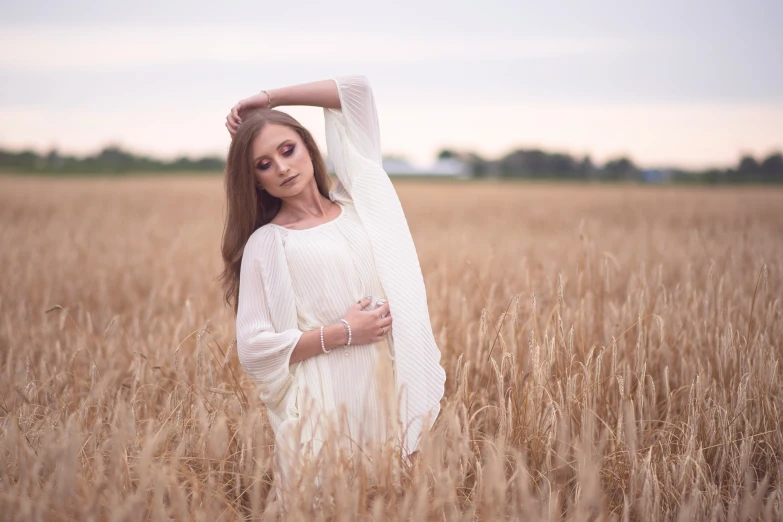 a woman wearing a white dress standing in a wheat field