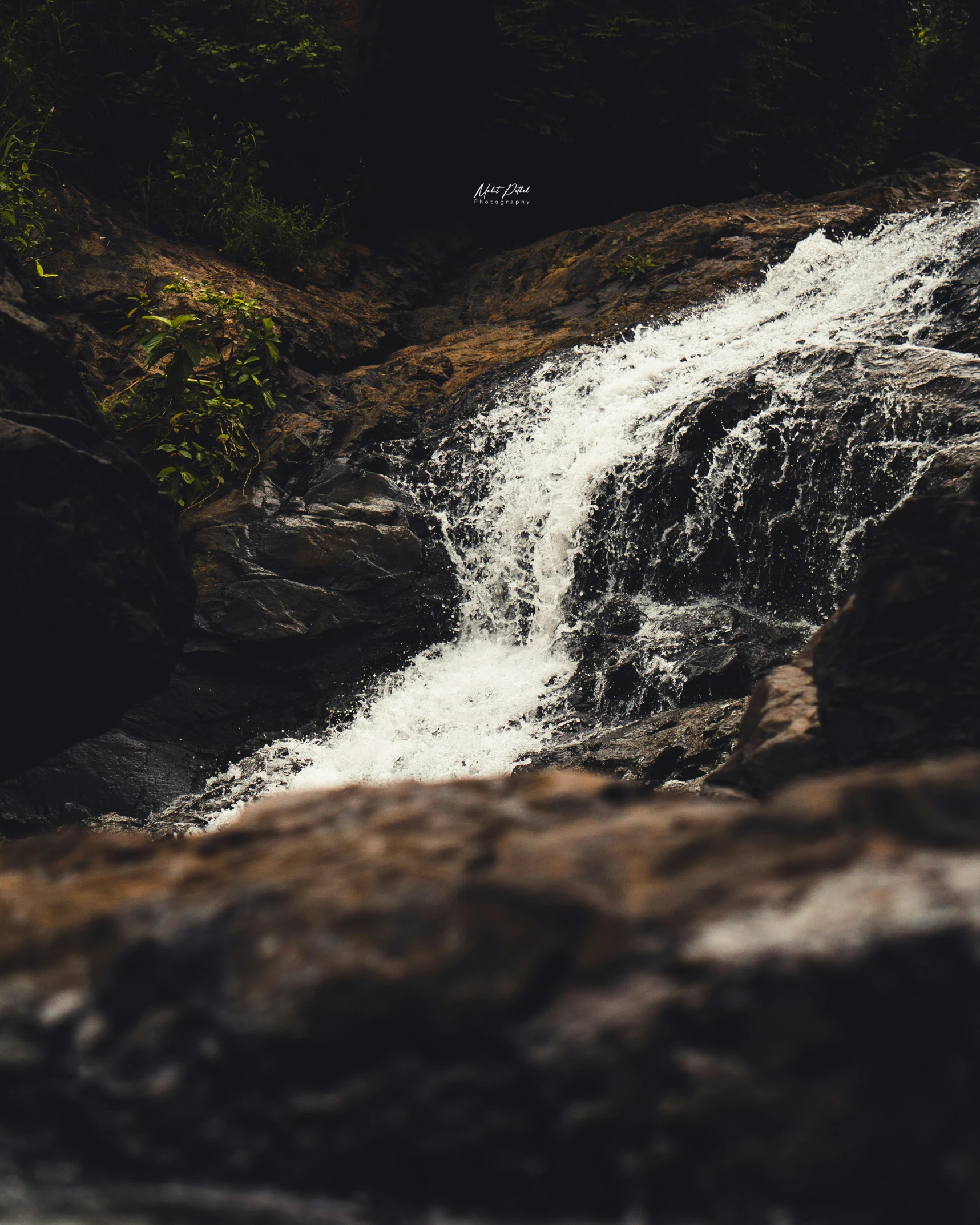 a waterfall next to rocks and grass