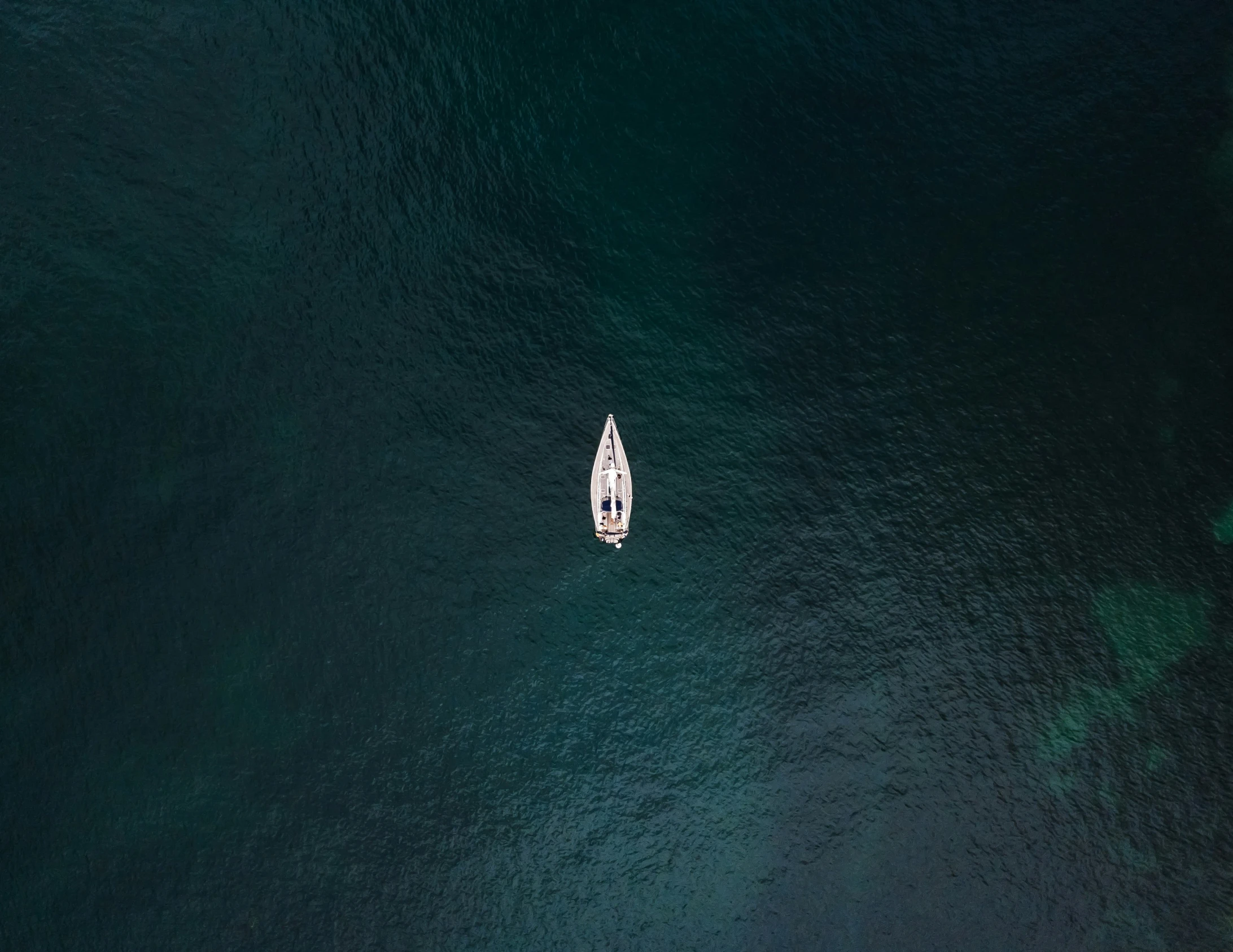 small white boat on calm water off a rocky coastline