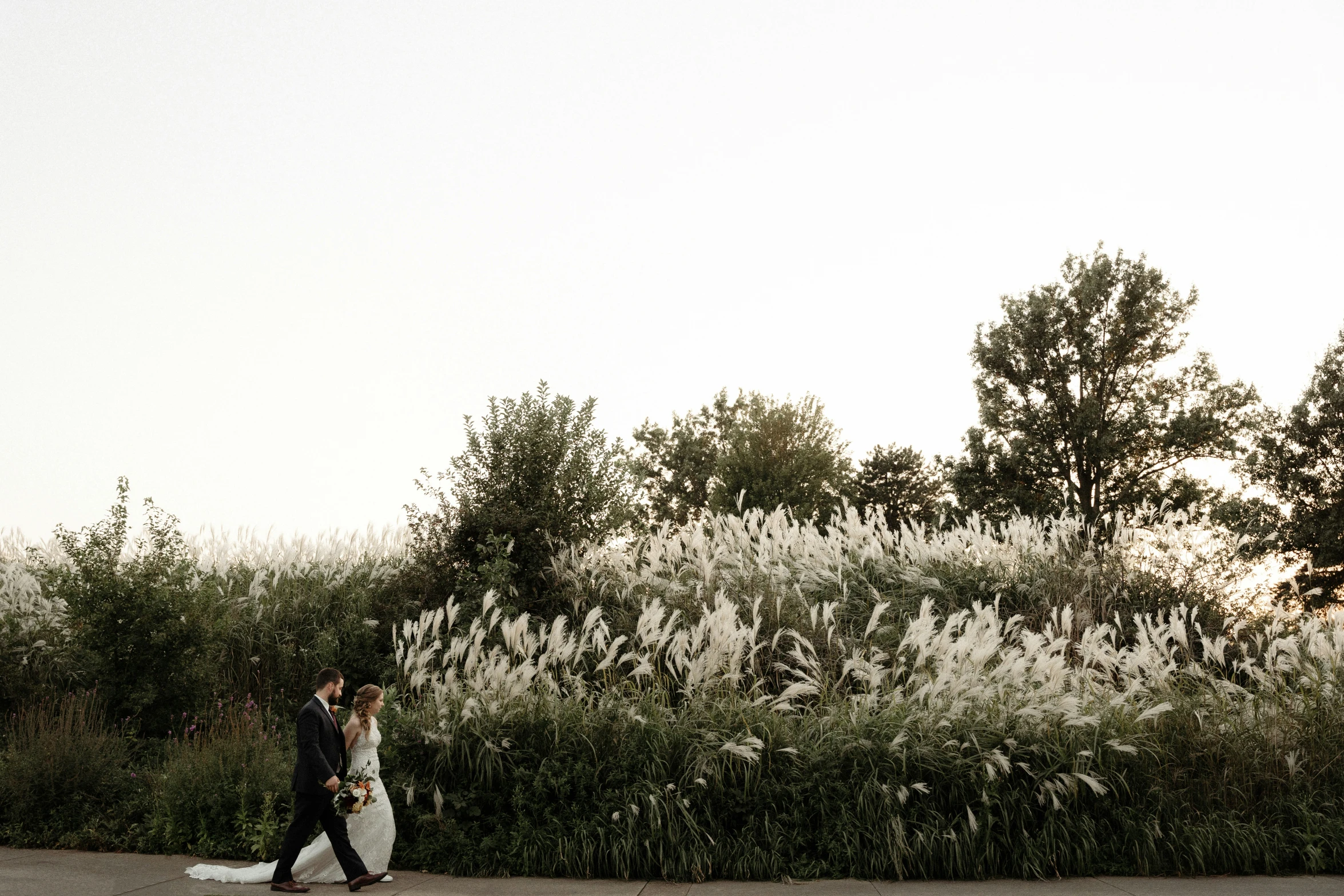 the man and woman are walking away from some tall grass