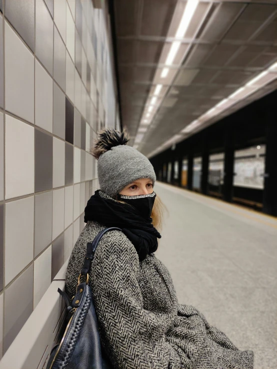 a woman wrapped in a coat sits in a subway station