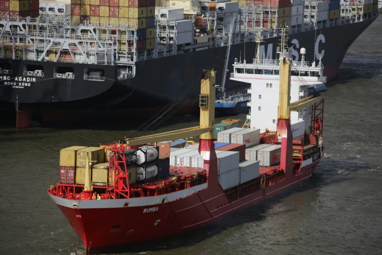 a red cargo ship is docked with multiple other boats