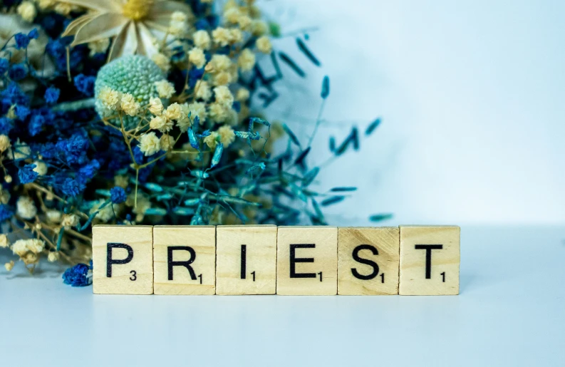 flowers and scrabble blocks spelling the word priest