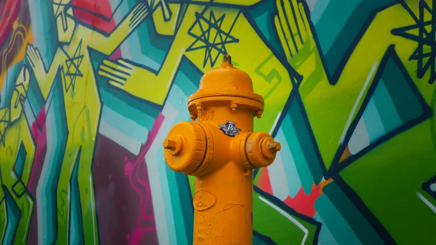 a yellow fire hydrant in front of graffiti painted walls