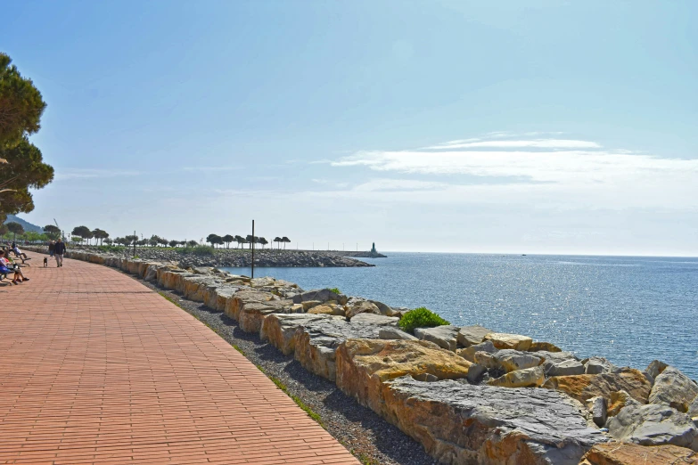 people are walking on the red pathway next to the ocean