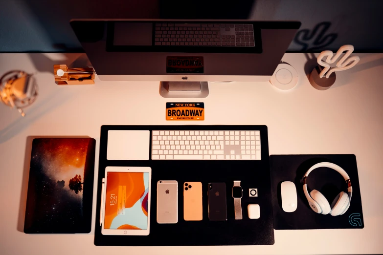 a laptop, phone, headphones, phone case and other items lay on a white desk