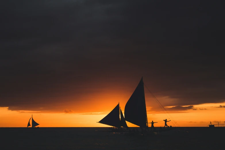 two sailboats in a calm ocean at sunset