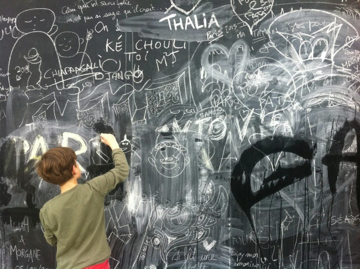 a boy writing on a chalkboard with some black spray paint