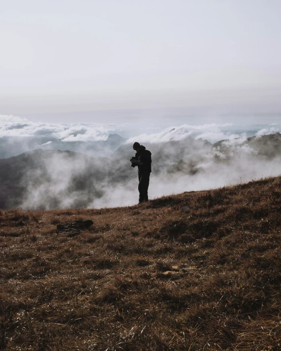 there is a man standing on a hilltop overlooking the clouds