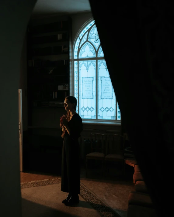 a woman standing in front of a window holding a cross