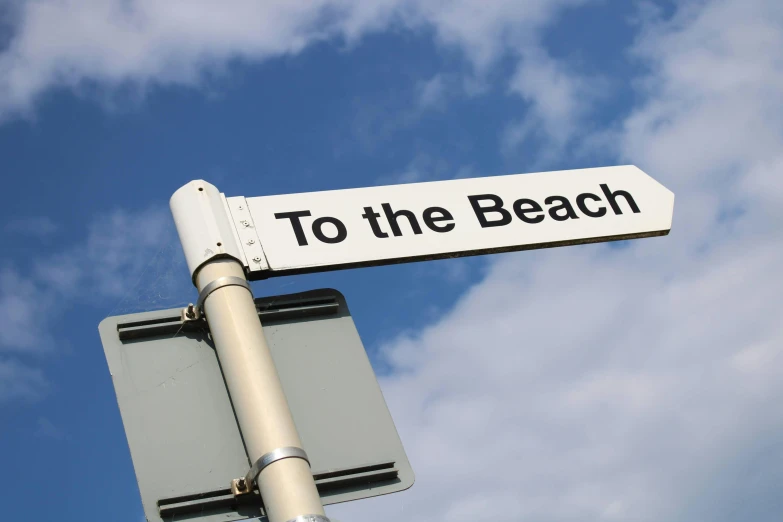 a street sign that reads to the beach under a cloudy blue sky