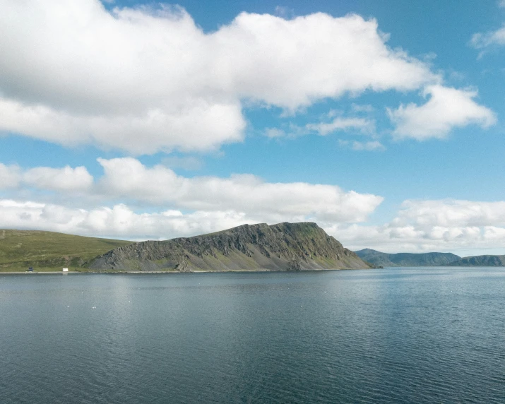 the island is near the water under a blue sky with clouds