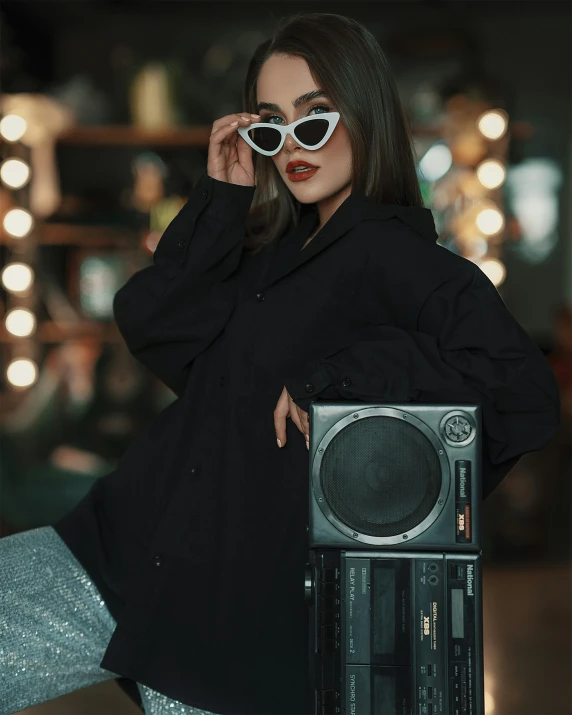 a woman in a black coat wearing glasses leaning on an old radio