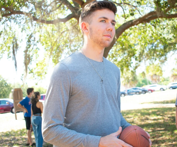 a young man holding a basketball while standing in a park