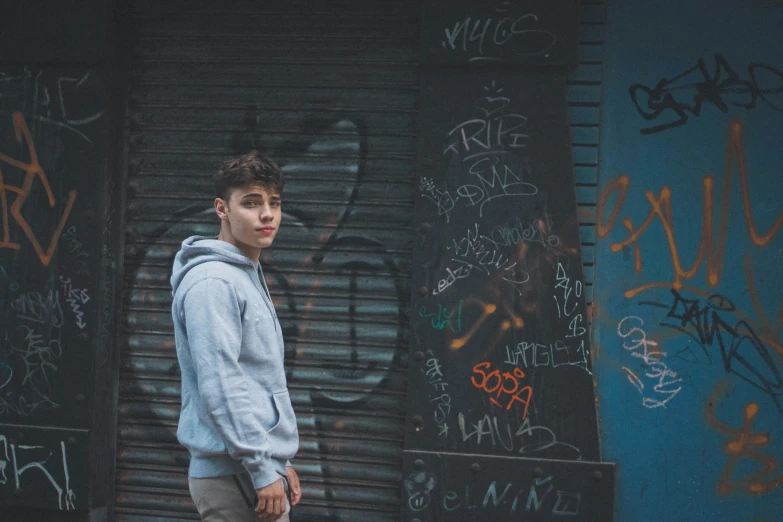 a young man is standing in front of a wall of graffiti