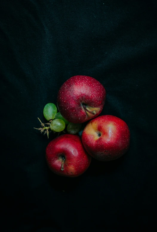 three red apples with green stem sitting on black cloth