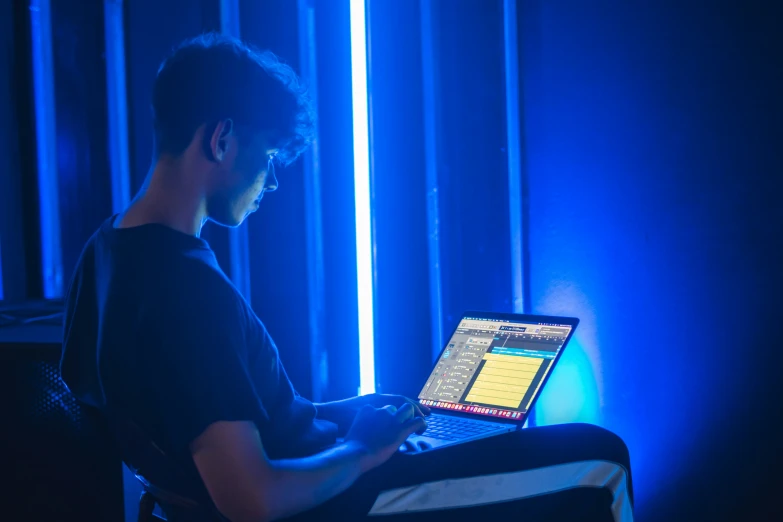 man sitting in chair holding laptop with blue light in room